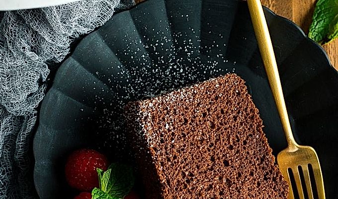 На черной матовой тарелке подают кусочек шоколадно-шифонового торта и малину.