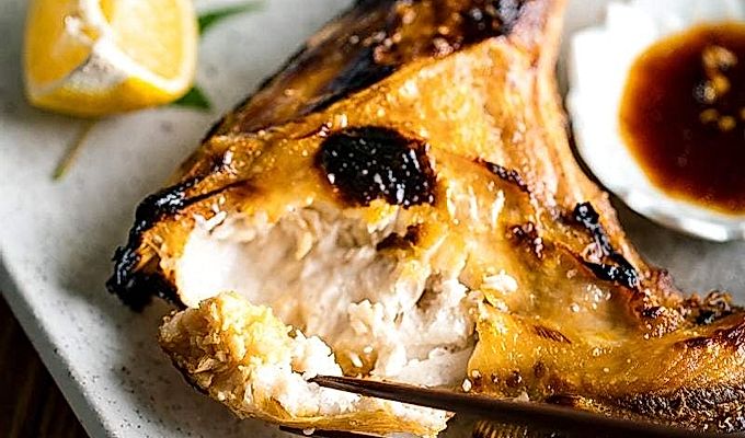 Белая японская керамическая тарелка, содержащая Hamachi Kama (ошейник из желтохвоста на гриле) вместе с долькой лимона и соевым соусом юдзу.
