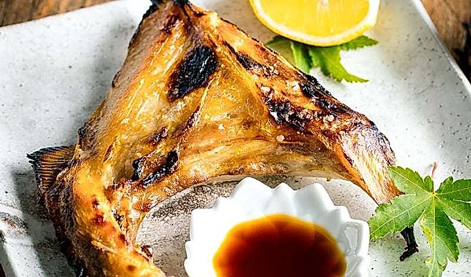 Белая японская керамическая тарелка, содержащая Hamachi Kama (ошейник из желтохвоста на гриле) вместе с долькой лимона и соевым соусом юдзу.