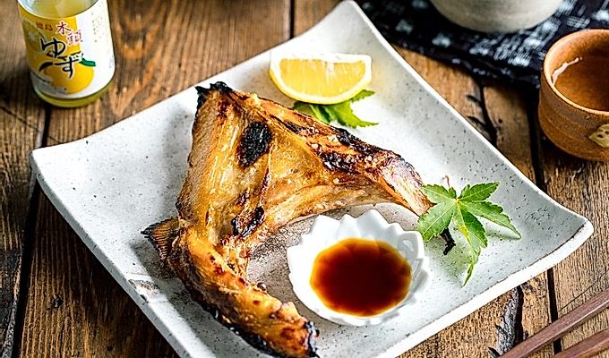 Белая японская керамическая тарелка, содержащая Hamachi Kama (ошейник из желтохвоста на гриле) вместе с долькой лимона и соевым соусом юдзу.