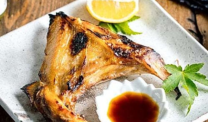 Белая японская керамическая тарелка, содержащая Hamachi Kama (ошейник из желтохвоста на гриле) вместе с долькой лимона и соевым соусом юдзу.
