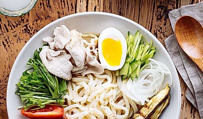 Белая миска с холодным карри удон, нарезанной свининой, вареным яйцом и свежими овощами.