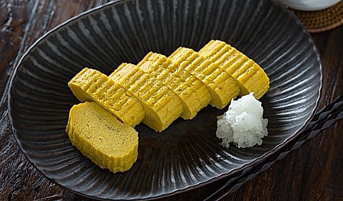 Tamagoyaki og revet daikon på en sort plade.