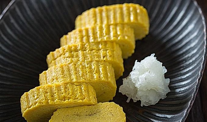 Tamagoyaki og revet daikon på en sort plade.