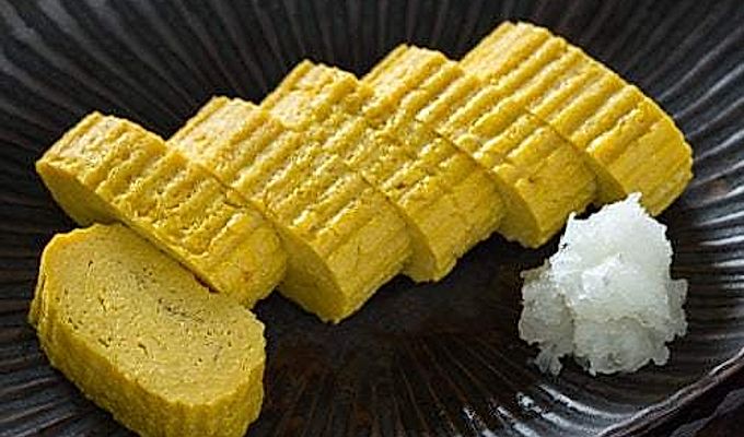 Tamagoyaki og revet daikon på en sort plade.