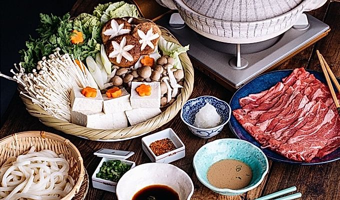 Tablesetup para sa shabu shabu - donabe hot pot, gulay, karne, udon, at paglubog ng sarsa.