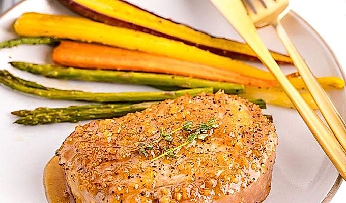 Белая тарелка, содержащая свиные отбивные с медом, чесноком, жареную морковь и спаржу.