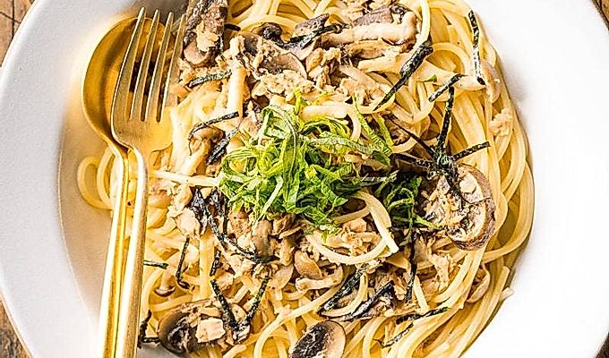 Een wit keramisch bord met tonijn-champignonpasta in Japanse stijl, gegarneerd met geraspte nori- en shiso-bladeren.