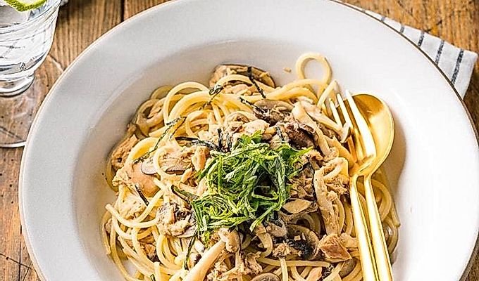 Een wit keramisch bord met tonijn-champignonpasta in Japanse stijl, gegarneerd met geraspte nori- en shiso-bladeren.