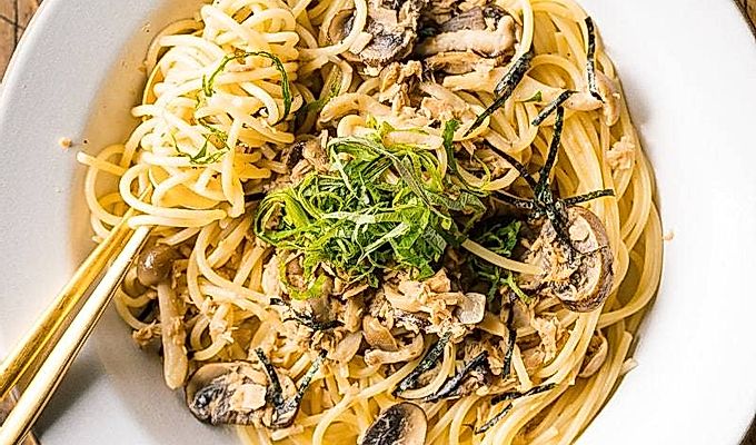 Een wit keramisch bord met tonijn-champignonpasta in Japanse stijl, gegarneerd met geraspte nori- en shiso-bladeren.