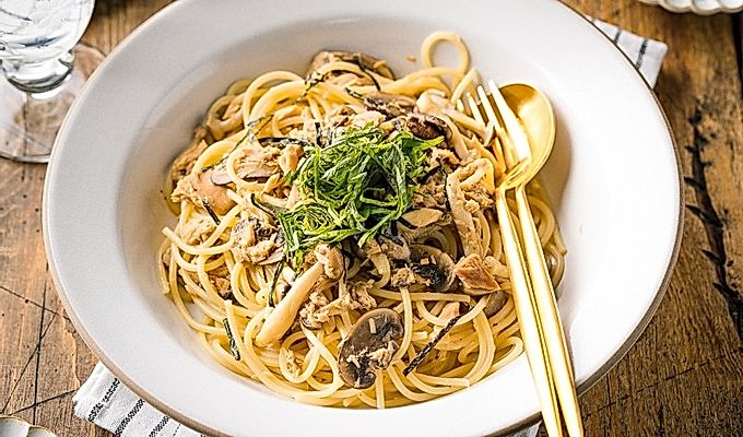 Een wit keramisch bord met tonijn-champignonpasta in Japanse stijl, gegarneerd met geraspte nori- en shiso-bladeren.