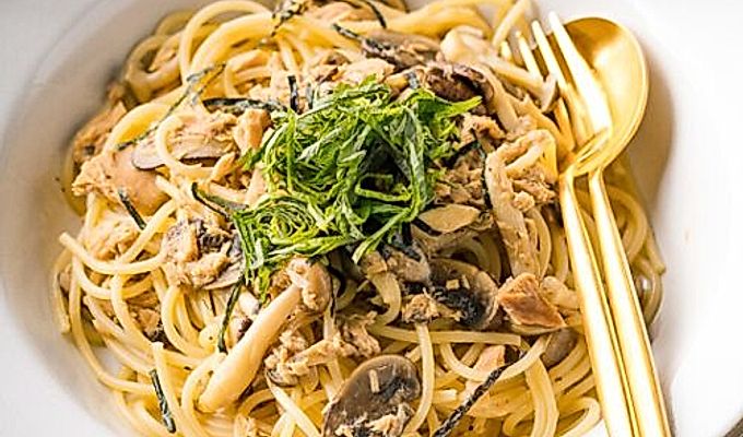 Een wit keramisch bord met tonijn-champignonpasta in Japanse stijl, gegarneerd met geraspte nori- en shiso-bladeren.