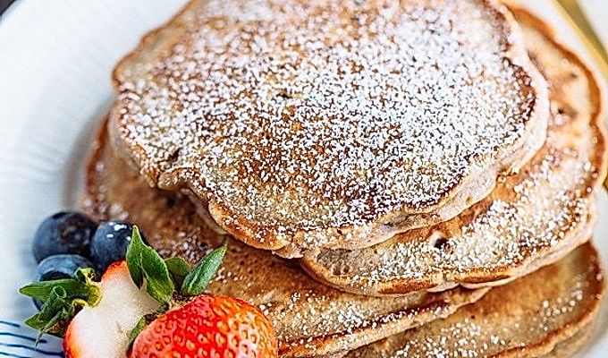 Pancake di fagioli rossi con fragole e mirtilli sul piatto bianco.