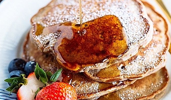Pancake di fagioli rossi con fragole e mirtilli sul piatto bianco.
