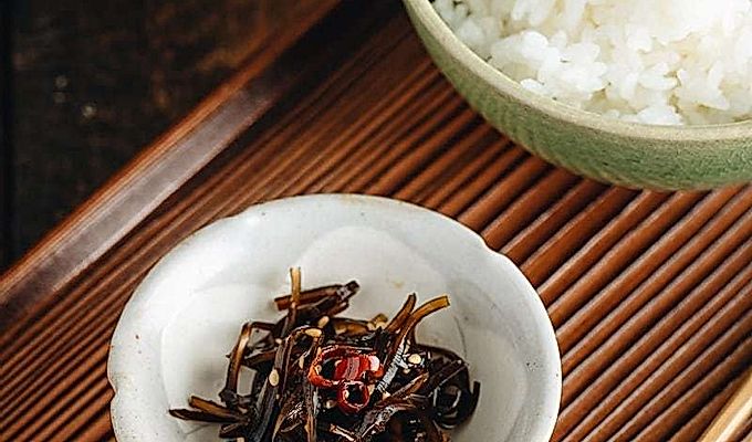 Kombu bollito in un piattino accanto a una ciotola di riso al vapore.