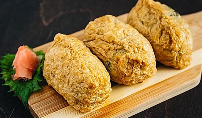 Inari Sushi podawane na desce wraz z marynowanym imbirem.