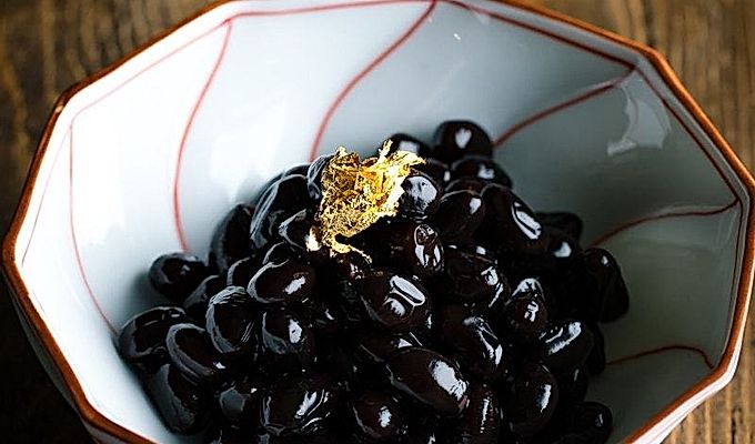 Japon yeni yıl kutlaması için altın varak ile tepesinde Kuromame, tatlı siyah soya fasulyesi içeren beyaz ve kırmızı bir Japon kasesi.