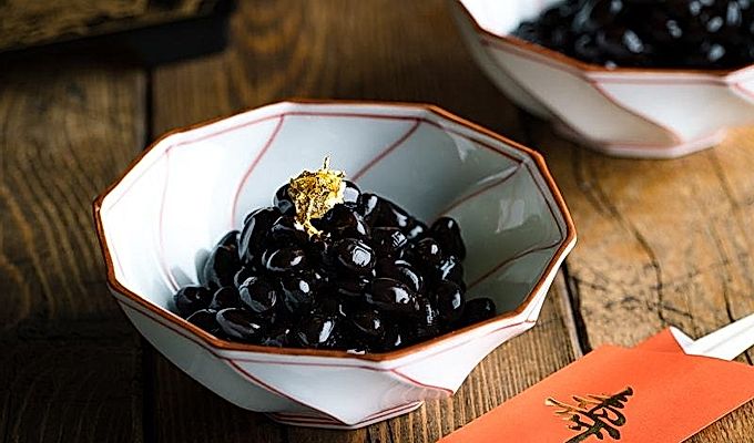 Japon yeni yıl kutlaması için altın varak ile tepesinde Kuromame, tatlı siyah soya fasulyesi içeren beyaz ve kırmızı bir Japon kasesi.