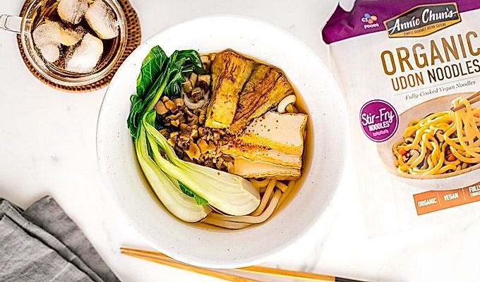 一个白色的碗,里面放着素食乌冬面汤,上面放着白菜、炸豆腐、碎米……