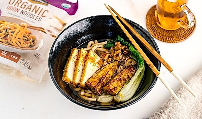 一个黑色的碗,里面放着素食乌冬面汤,上面放着白菜、炸豆腐、碎米……