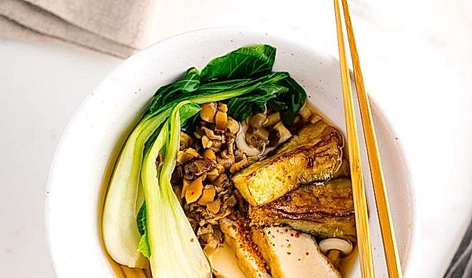 一个白色的碗,里面放着素食乌冬面汤,上面放着白菜、炸豆腐、碎米……