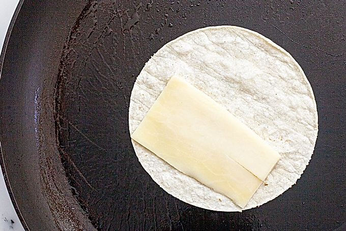 Маленькая лепешка на сковороде с сыром на половине, чтобы приготовить вегетарианский рецепт тако.