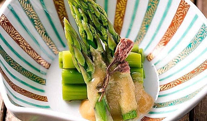 Un cuenco con forma de concha que contiene espárragos con aderezo de miso (Karashi Sumisoae) aderezado con flor de cerezo en escabeche con sal.