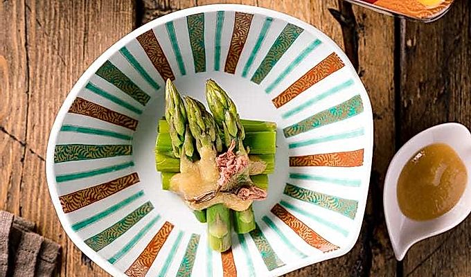 Un cuenco con forma de concha que contiene espárragos con aderezo de miso (Karashi Sumisoae) aderezado con flor de cerezo en escabeche con sal.