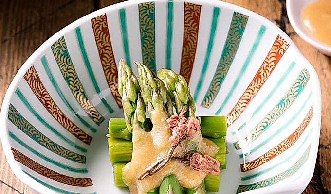 Un cuenco con forma de concha que contiene espárragos con aderezo de miso (Karashi Sumisoae) aderezado con flor de cerezo en escabeche con sal.