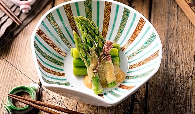 Un cuenco con forma de concha que contiene espárragos con aderezo de miso (Karashi Sumisoae) aderezado con flor de cerezo en escabeche con sal.