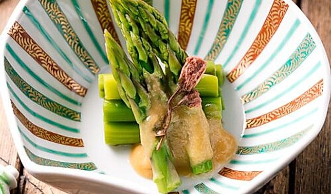 Un cuenco con forma de concha que contiene espárragos con aderezo de miso (Karashi Sumisoae) aderezado con flor de cerezo encurtida con sal.