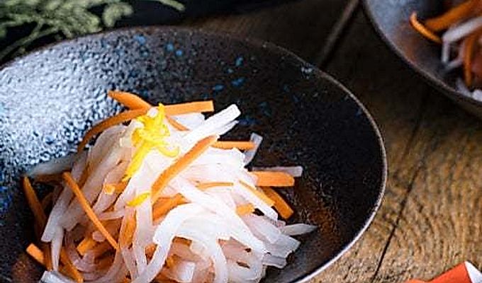 Черная миска, содержащая Намасу (японский дайкон и морковный салат).