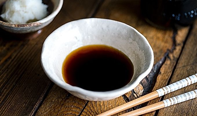 Valkoinen kulho, joka sisältää Tempura-kastoskastiketta (Tentsuyu), tarjoillaan raastetun daikonin kanssa.