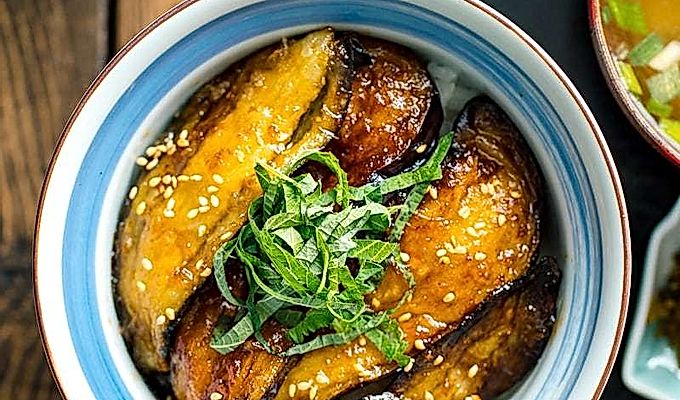 Uma tigela de arroz japonesa contendo Soja Berinjela Vitrificada Donburi coberta com shiso juliana e sementes de gergelim torradas.