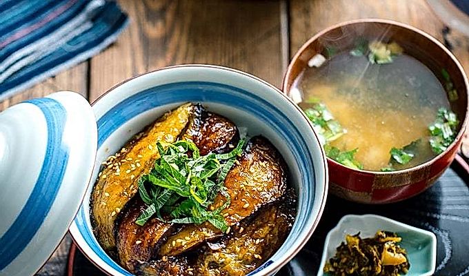 Uma tigela de arroz japonesa contendo Soja Berinjela Vitrificada Donburi coberta com shiso juliana e sementes de gergelim torradas.