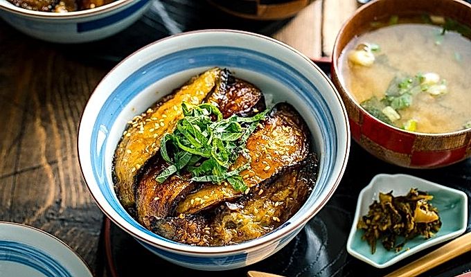 Uma tigela de arroz japonesa contendo berinjela donburi com cobertura de soja coberta com shiso juliana e sementes de gergelim torradas.