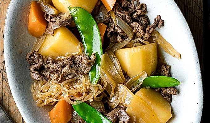 Белая овальная тарелка с Nikujaga (японское тушеное мясо и картофель).