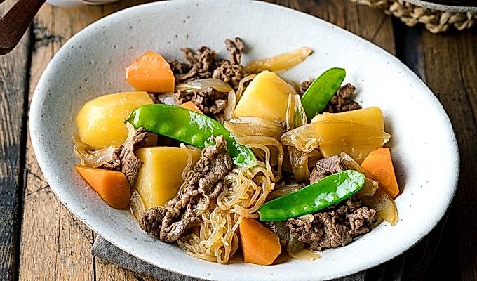 Белая овальная тарелка с Nikujaga (японское тушеное мясо и картофель).