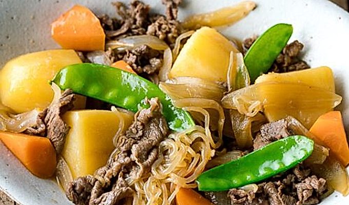 Белая овальная тарелка с Nikujaga (японское тушеное мясо и картофель).