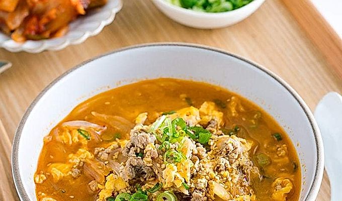 Белая миска с супом из кимчи, приготовленным из стеклянной лапши Мэлони, кимчи, яиц и свинины.